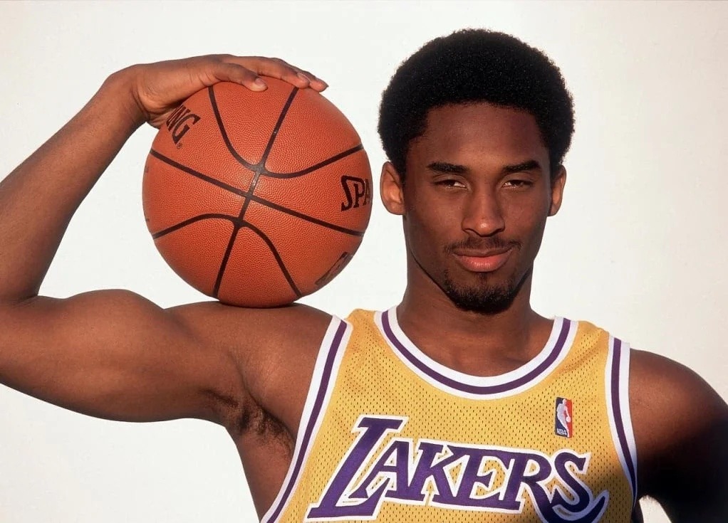Young Kobe Bryant in a gold Lakers jersey holding a basketball on his shoulder in his 1996 rookie photo shoot