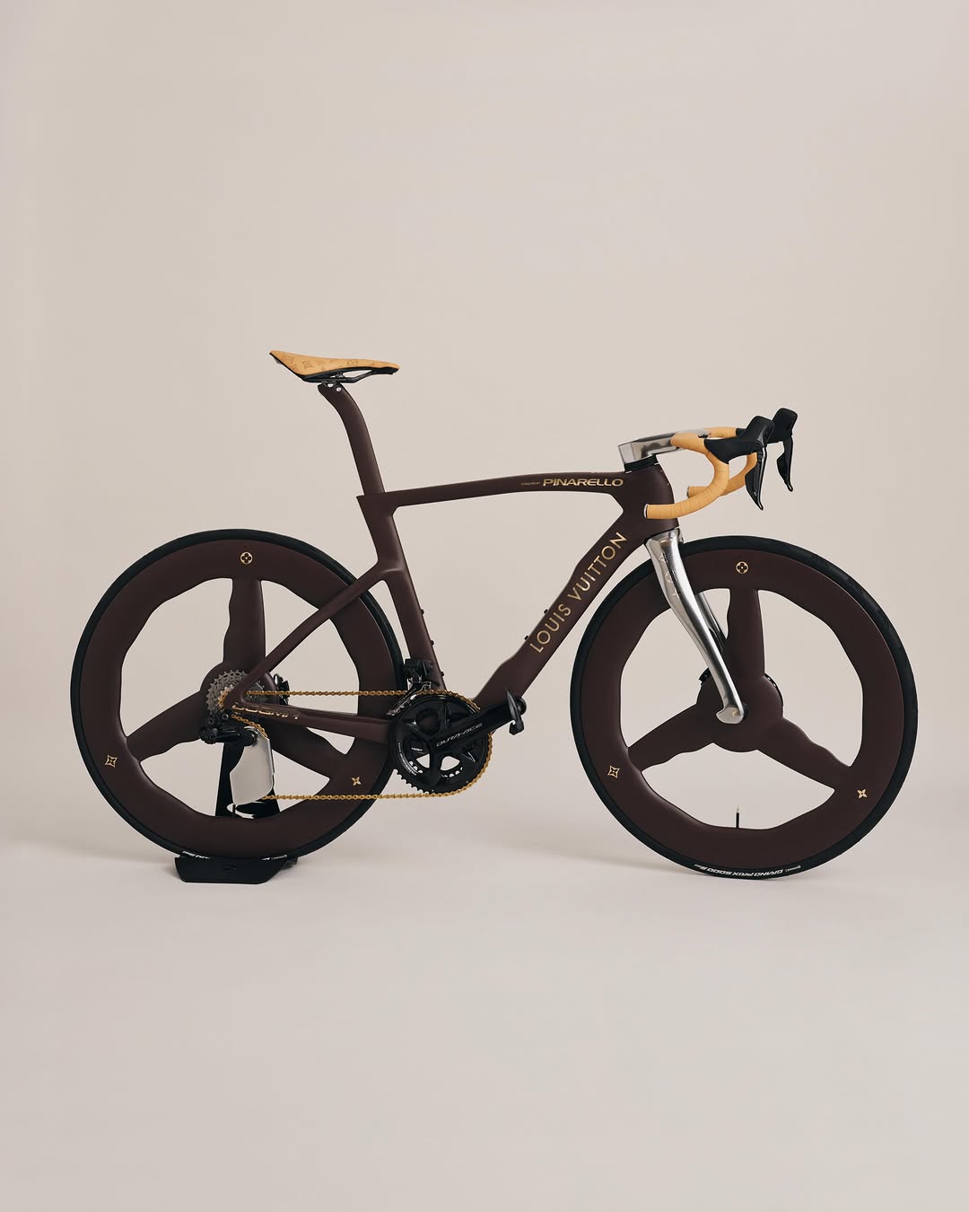 A model carries the brown Louis Vuitton Pinarello Dogma F bike over one shoulder on the SS27 sand runway