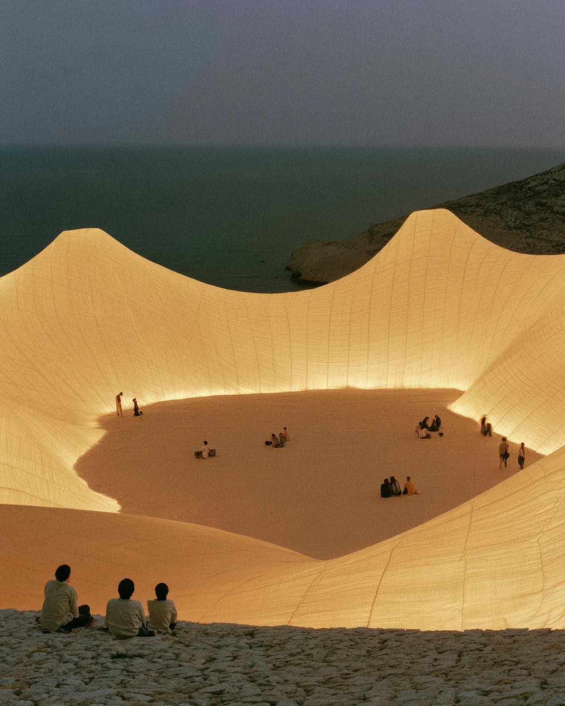 A rendered amber lit canopy stretching from a beach into calm sea water at sunset, part of Marius Troy's imagined Le Festival du Soleil series.