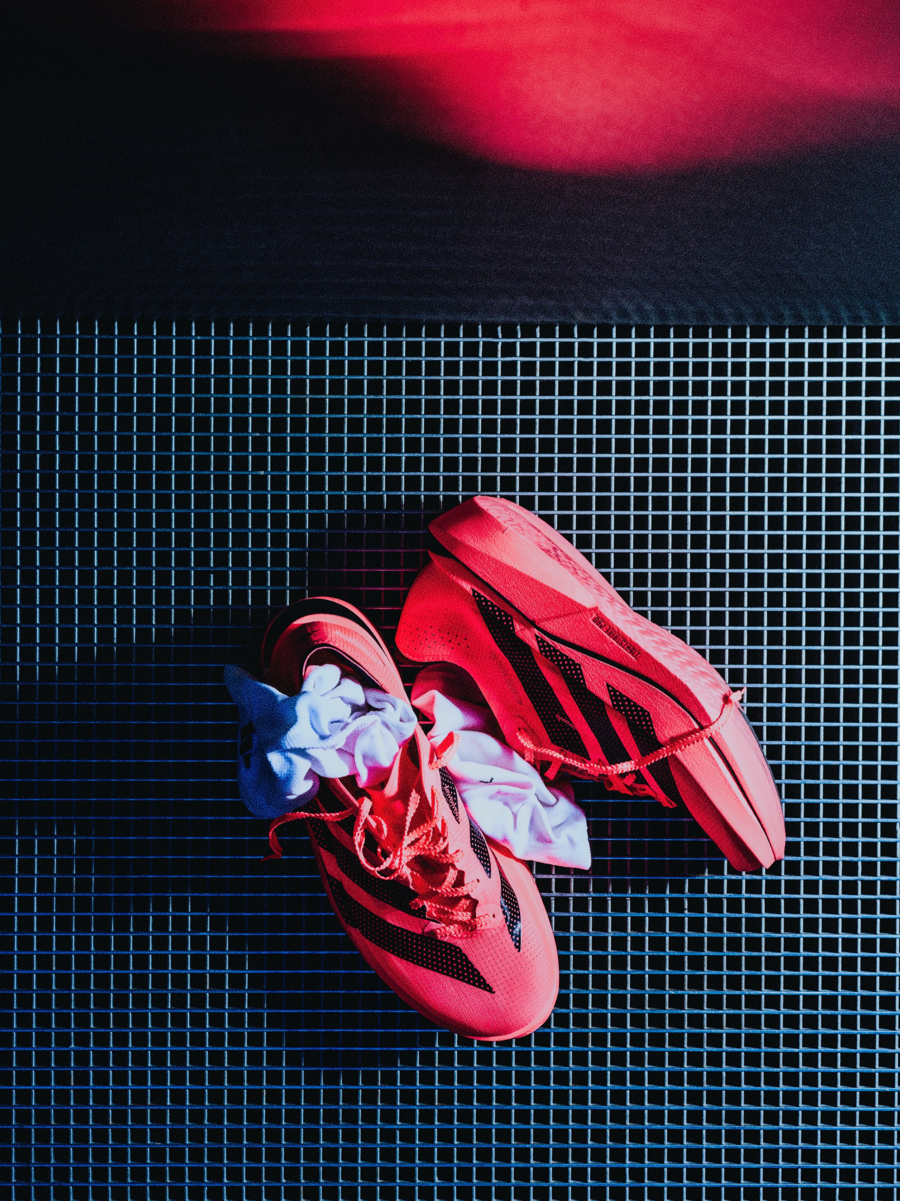 Coral Adidas Adios Pro 5 running shoes on a metal mesh surface.