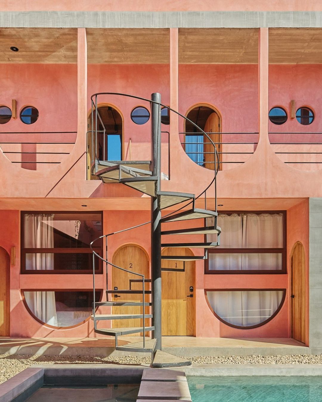 Pink arches and a slender spiral stair frame Amplitude Coliving’s courtyard.