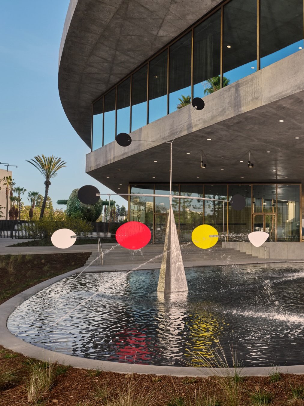 A Calder standing mobile sculpture with paddle shaped blades rises from a reflecting pool in front of LACMA's galleries.