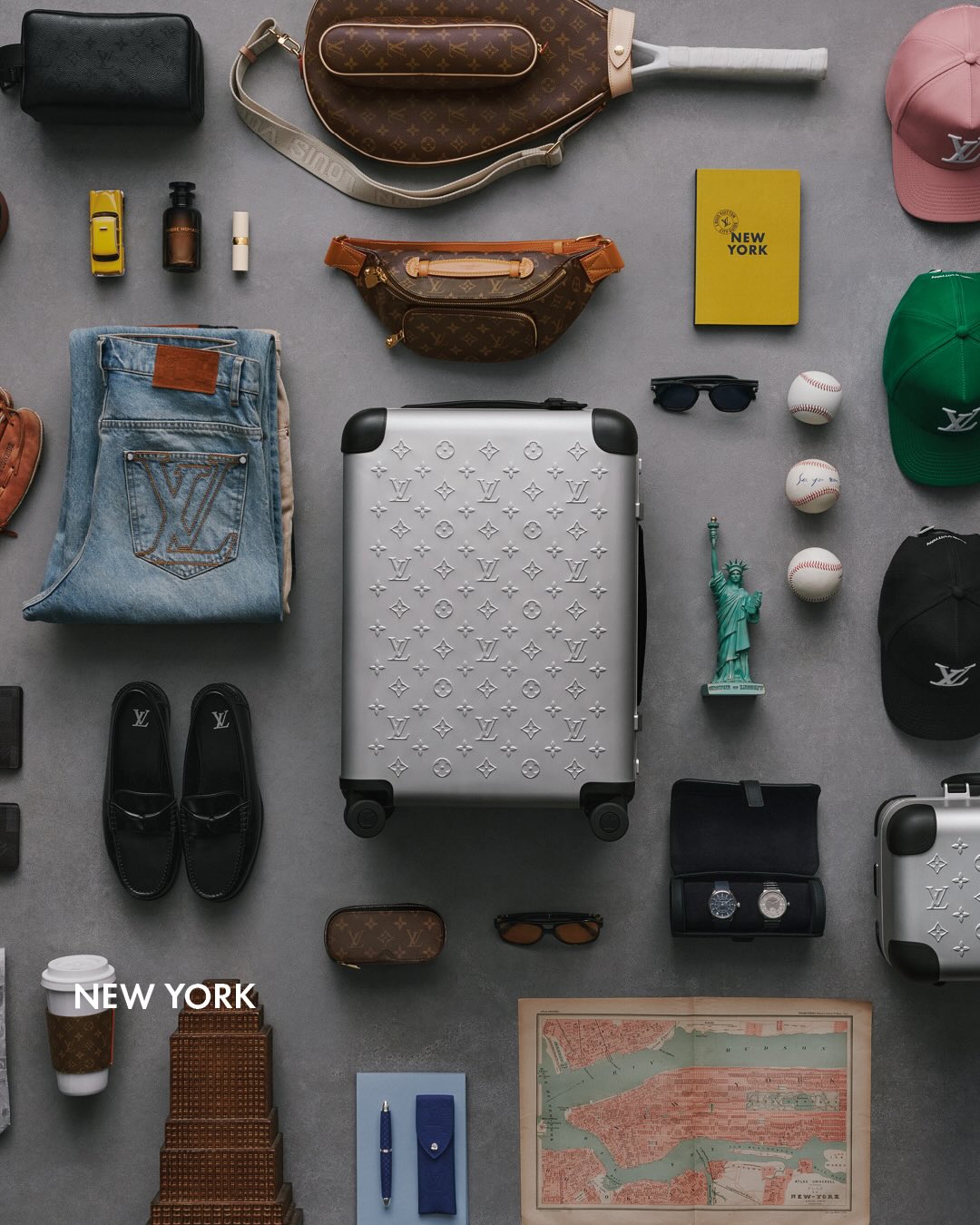 A Louis Vuitton aluminium Horizon suitcase arranged with travel belongings in an overhead city themed composition.