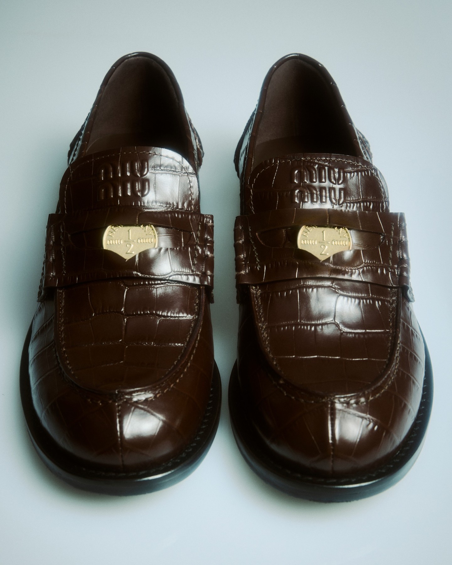 Brown stamped Miu Miu loafers feature broad straps and small metal ornaments.