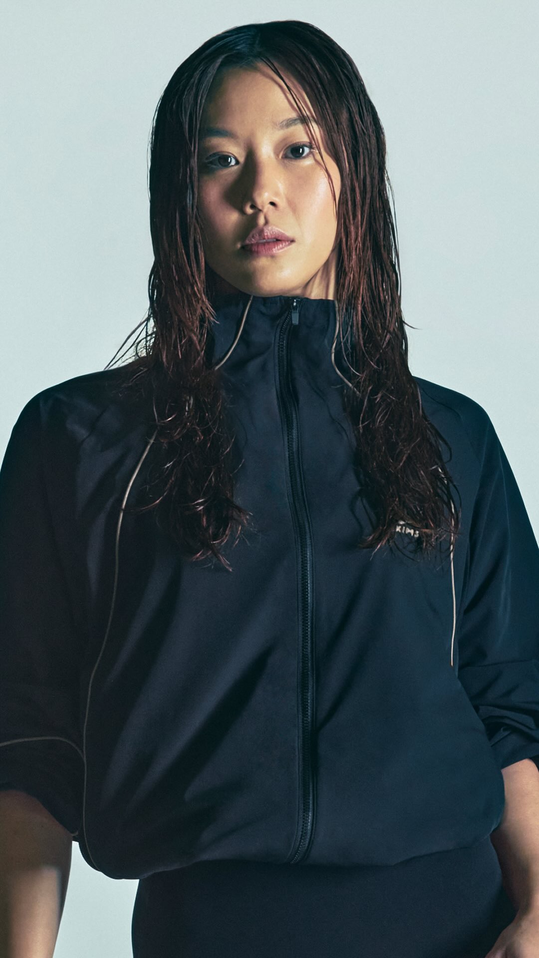 Stephanie Au wearing a dark NikeSKIMS jacket zipped high, with wet hair swept back.