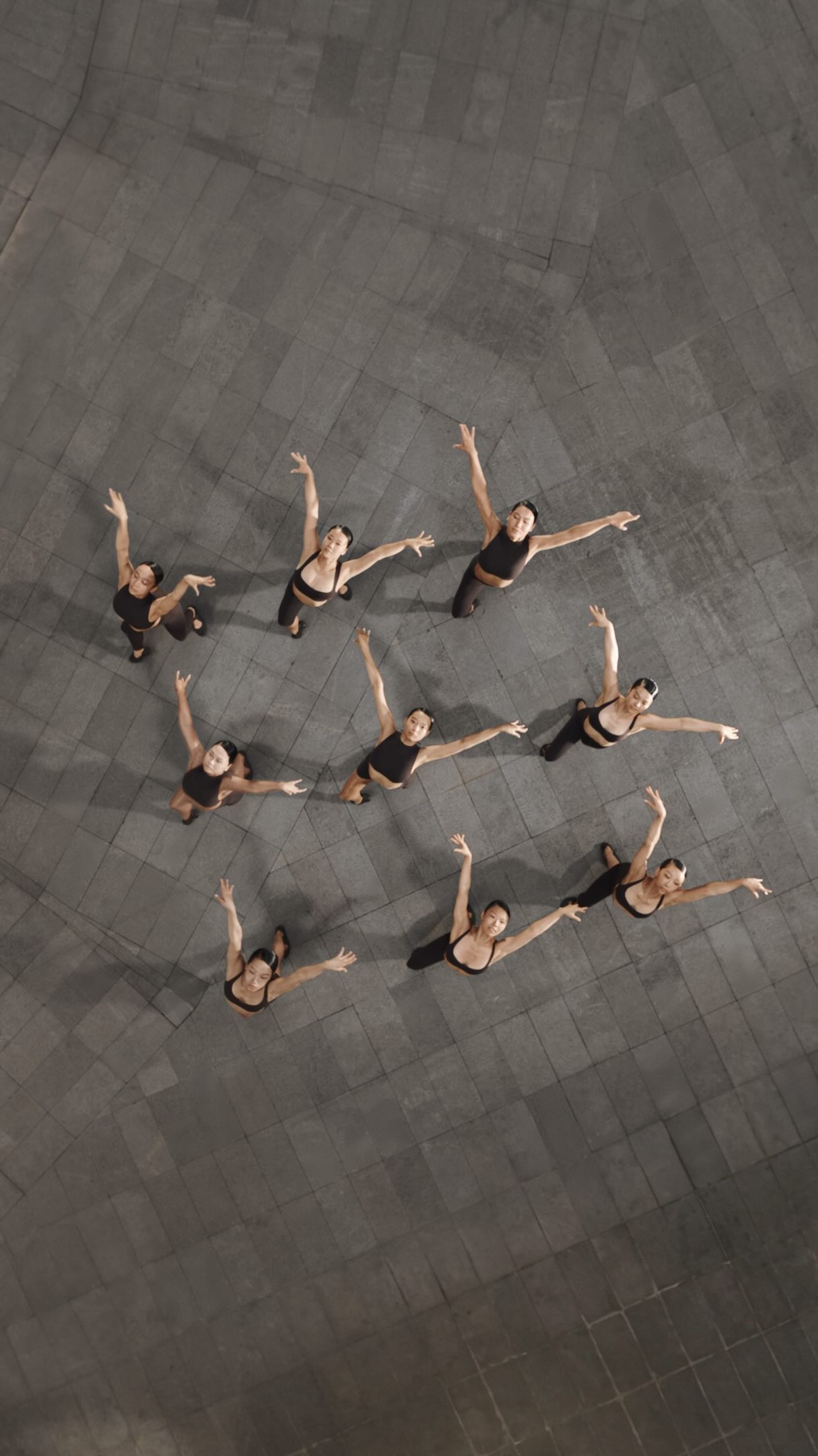 Dancers in dark NikeSKIMS clothing form a group within a pale architectural setting.