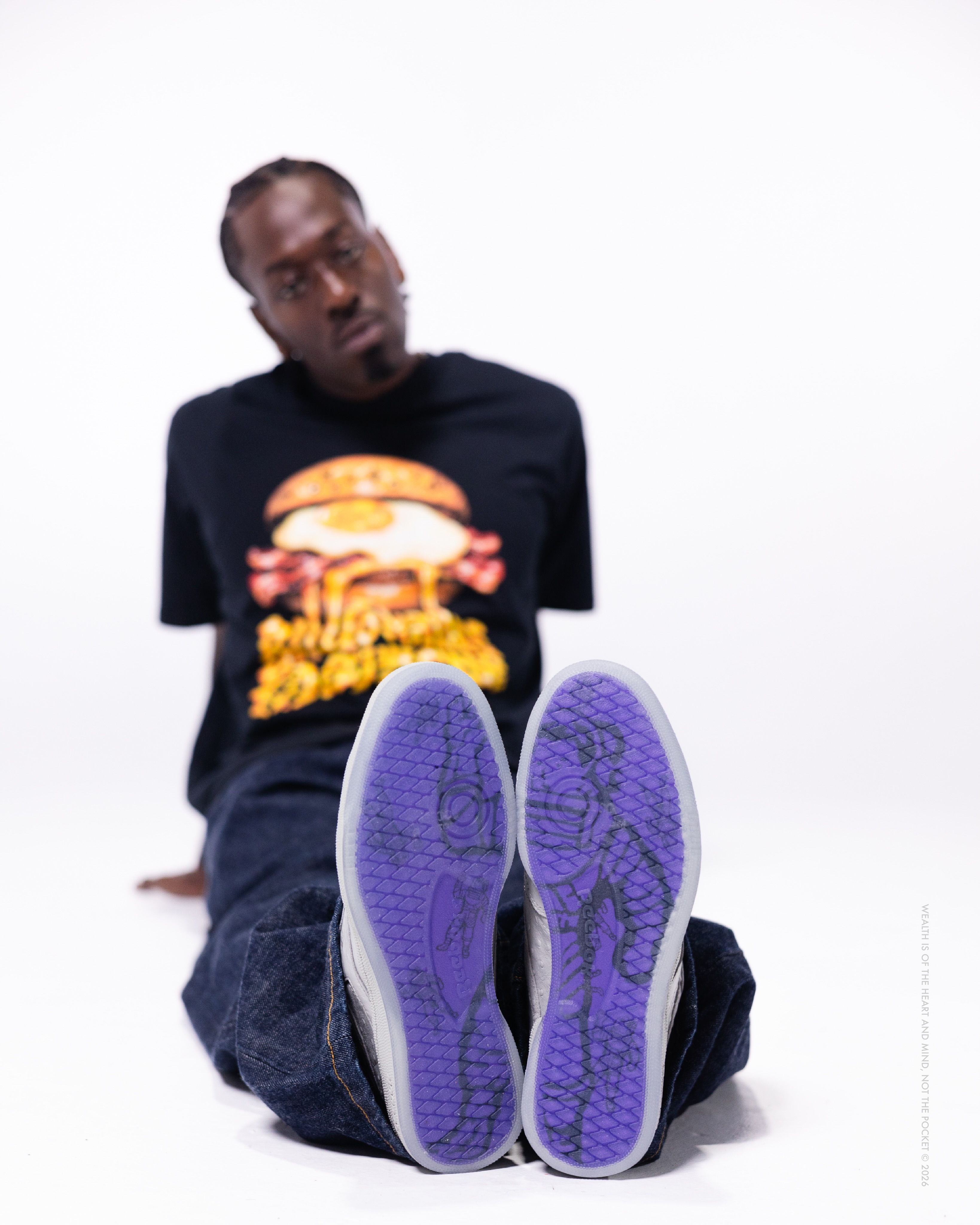 Grey textured BBC Reebok Club C 85 shoes with purple tinted soles beneath loose denim.
