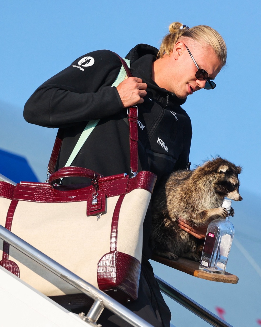 Erling Haaland carries a taxidermied raccoon and a Dolce and Gabbana tote bag while arriving at Oslo airport after Norways 2026 World Cup quarterfinal exit.