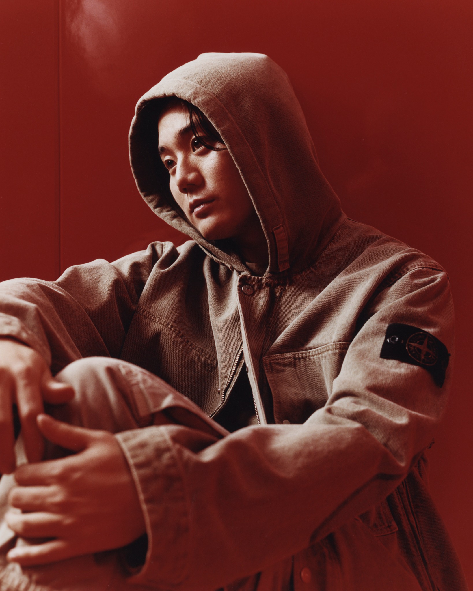 Simjae photographed behind the scenes wearing Stone Island's Q100045 Mineral Dyed Cotton Gabardine hooded jacket during the Autumn Winter 2026 campaign.