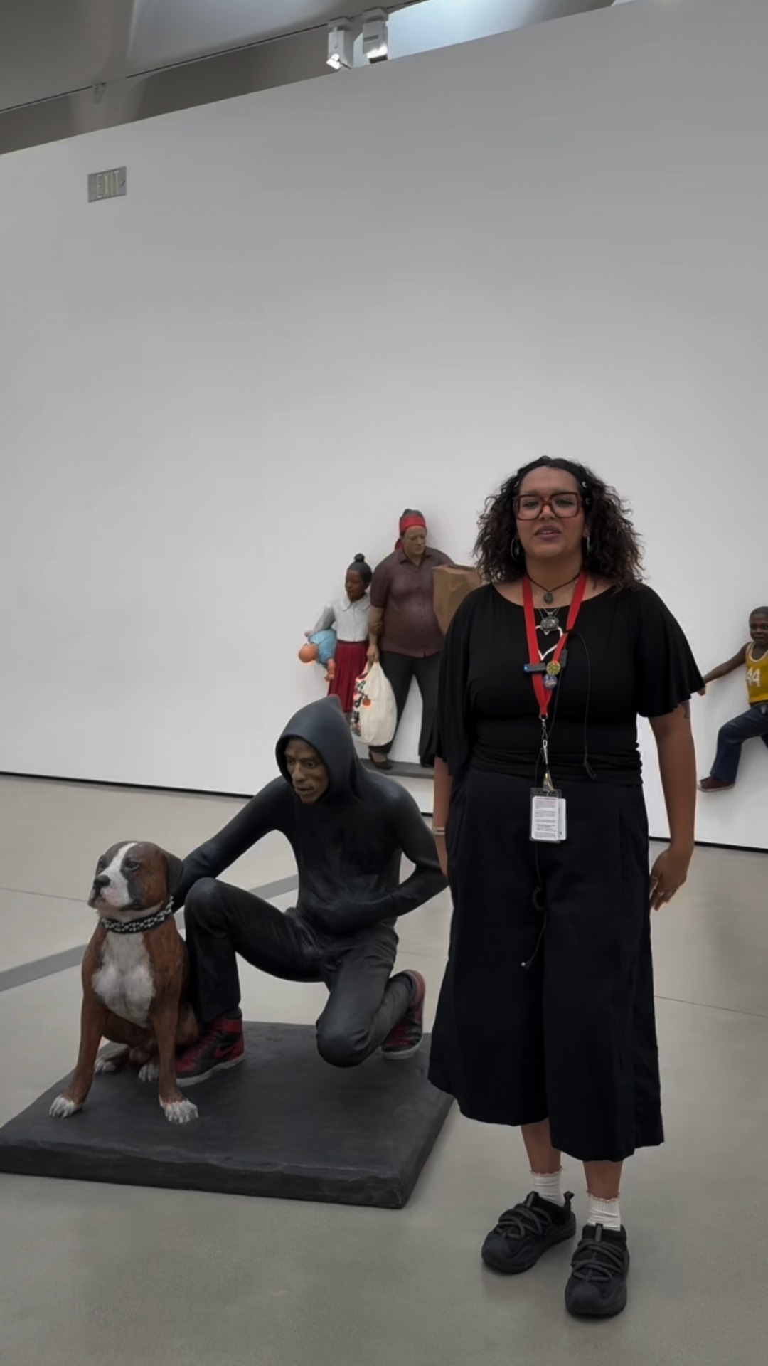 A Broad Visitor Experience staff member stands beside figurative sculptures.
