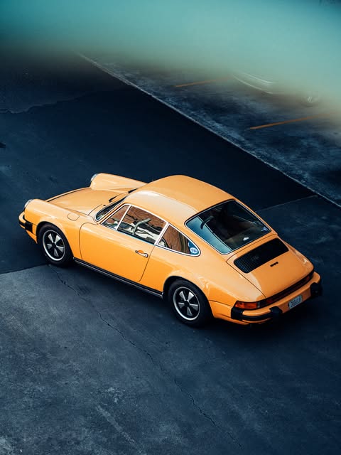 A Talbot Yellow 1977 Porsche 911 2.7 mid year parked on a rural road.