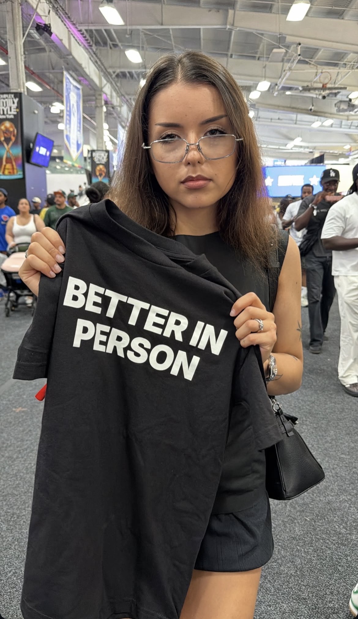Lexa Gates holding up a black Better in Person T-shirt at Complex Family Style in New York