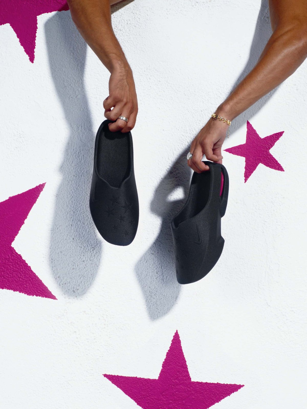 Masyn's black 3D printed Air Max mules held over a floor painted with pink stars.