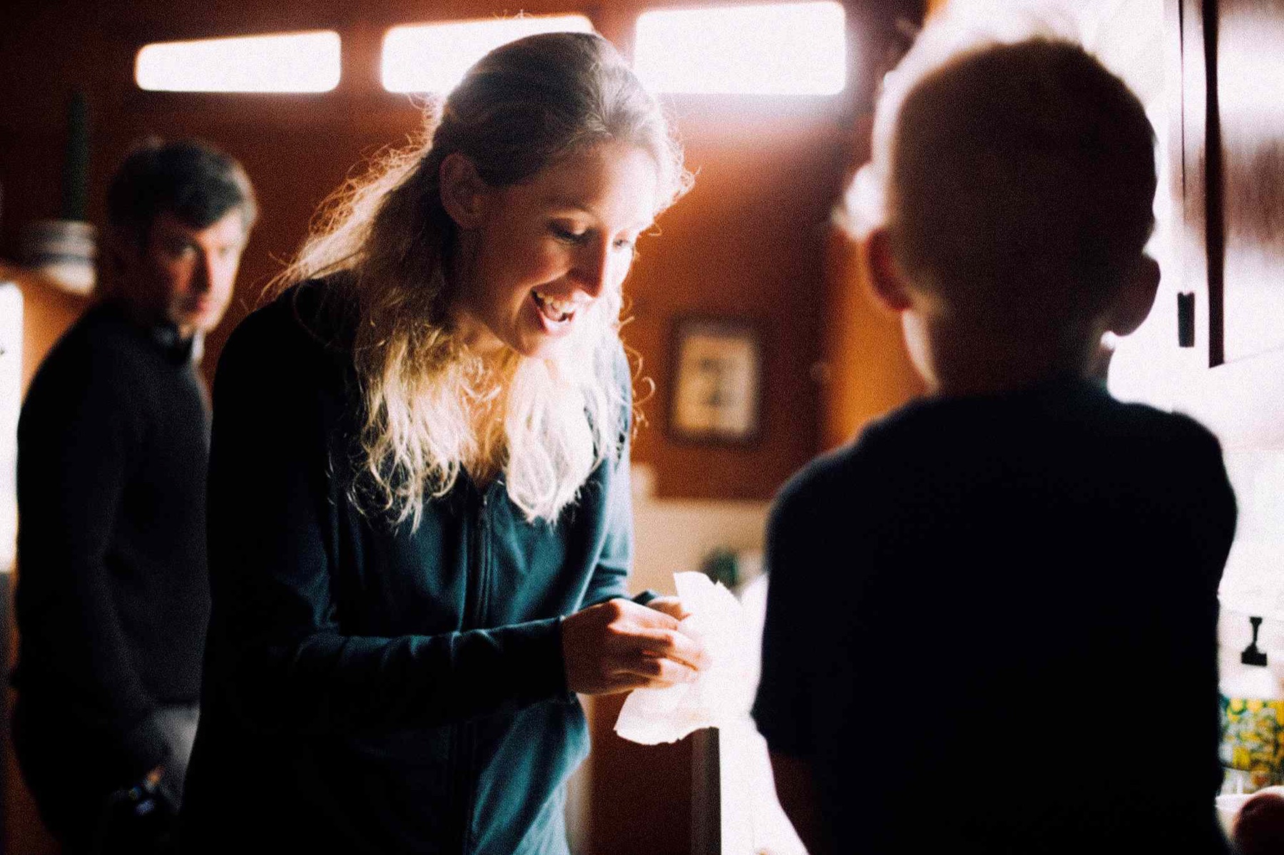 Elizabeth Holmes laughing in a kitchen with Nathan Fielder standing behind her in a still from the A24 documentary You Can See Everything