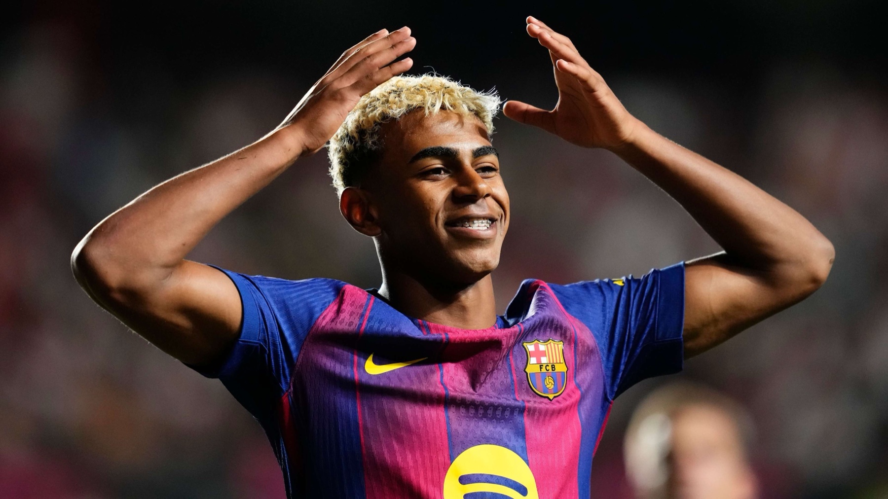 Lamine Yamal celebrating in a Barcelona home jersey, hands raised above his head, smiling