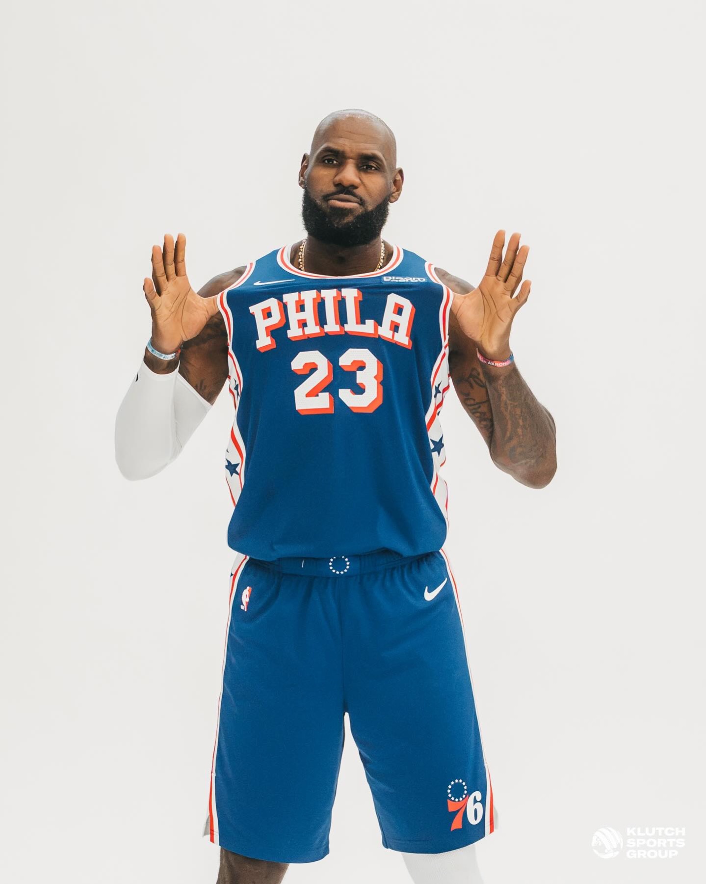 LeBron James in a blue Philadelphia 76ers number 23 jersey with both hands raised