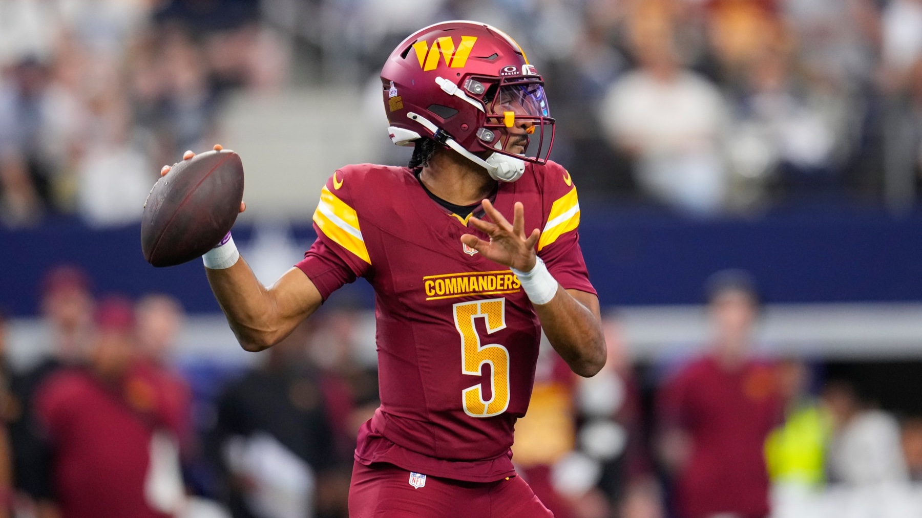 Commanders quarterback Jayden Daniels in a burgundy number 5 jersey setting up to throw