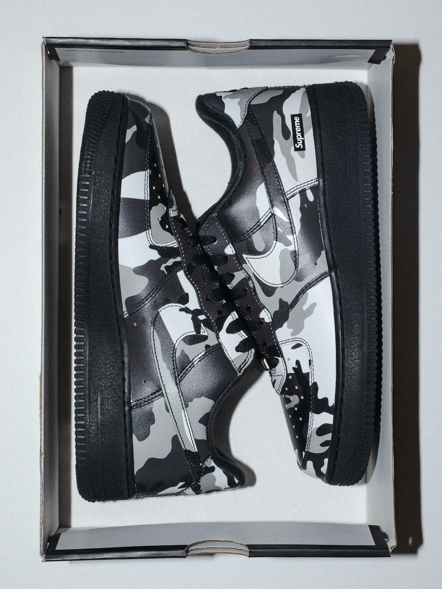 Supreme Nike Air Force 1 Low in black, white and gray camo with a black sole, shown in its box.